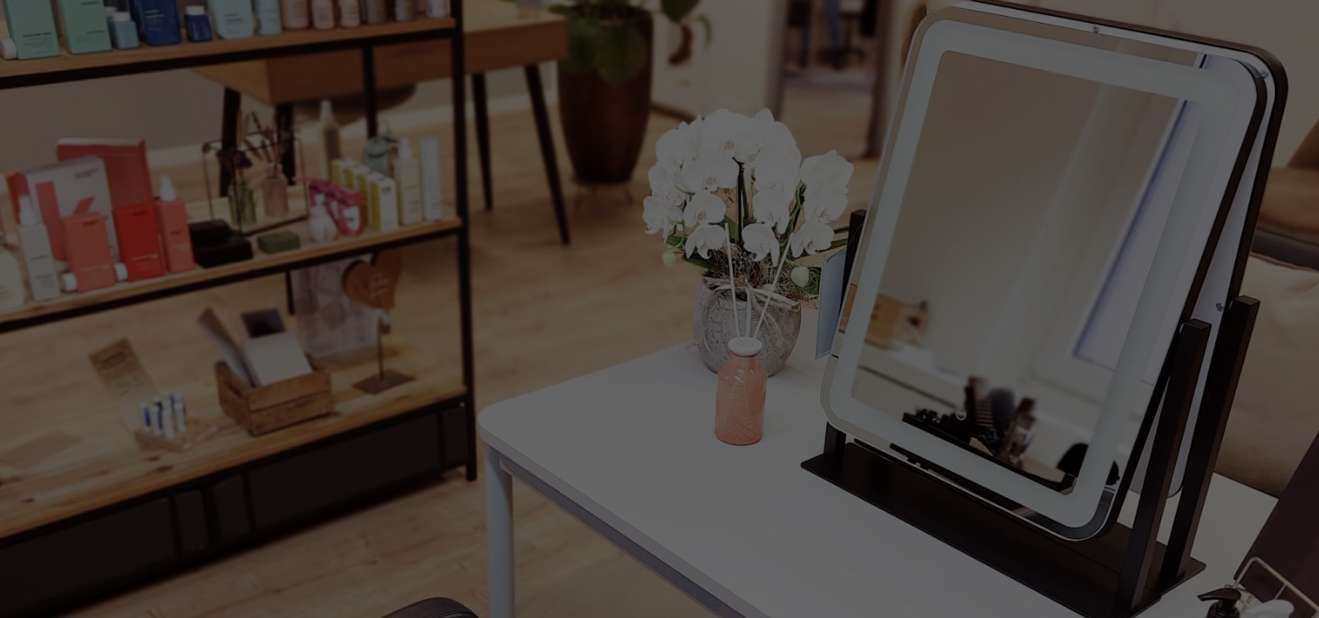 Ein Spiegel mit integrierter Belichtung, der auf einem Tisch neben einer Blumenvase und einem Lufterfrischer steht. Im Hintergrund ein Regal mit verschiedenen Kevin Murphy Haarpflegeprodukten